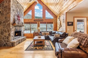 Un salon chaleureux avec une cheminée en pierre, des canapés en cuir et de grandes fenêtres donnant sur une vue imprenable sur les montagnes.