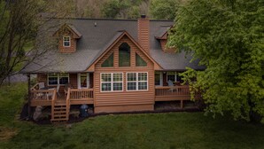 A log cabin with a front porch, large windows, and a chimney. - Riverfront cabin, arcade, hot tub, pool, trout fishing, pet friendly (Hiawassee)