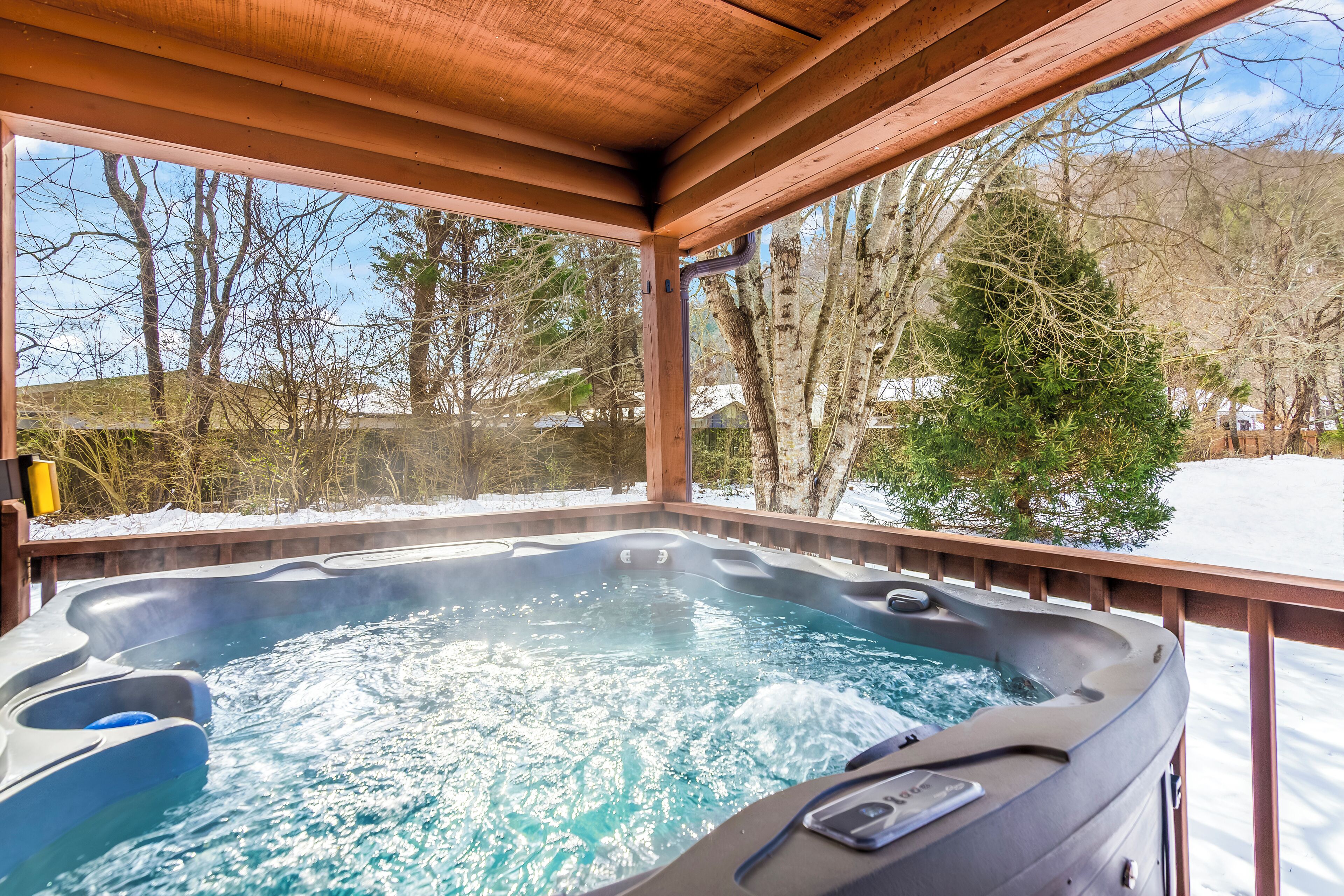 Un bain à remous avec une terrasse en bois et une vue sur les arbres et un paysage enneigé.