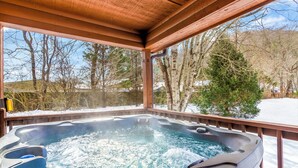 A hot tub with a wooden deck and a view of trees and a snowy landscape. - Riverfront cabin, arcade, hot tub, pool, trout fishing, pet friendly (Hiawassee)