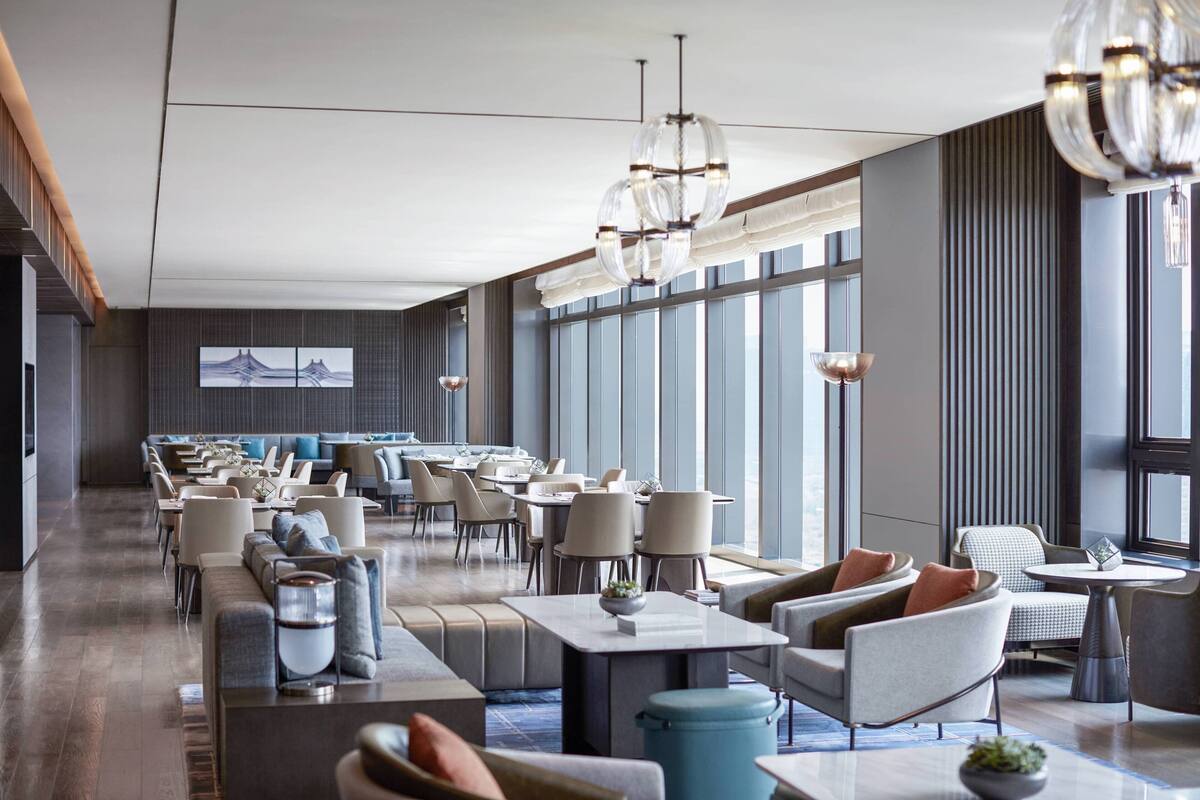A modern hotel lobby with a long reception area, multiple seating options, and large windows providing natural light.