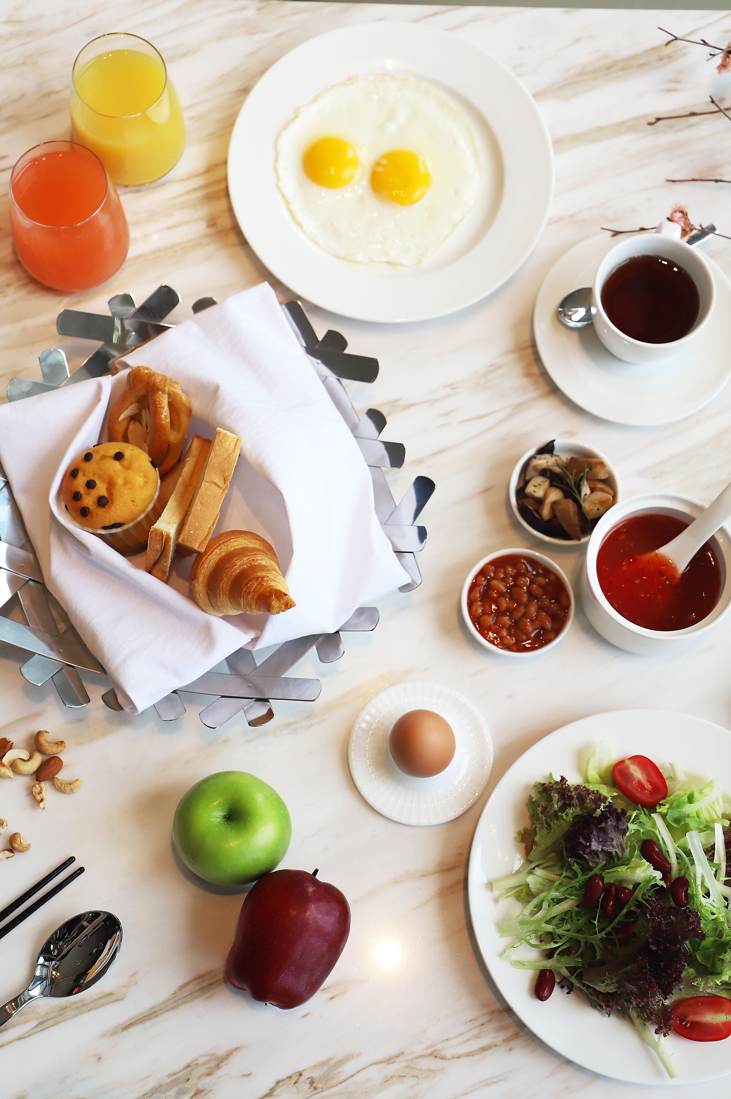 Een ontbijttafel met een croissant, muffin en appel, samen met een bord eieren en een salade.