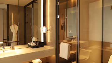 Un baño moderno con cabina de ducha de vidrio, un espejo grande y un lavamanos blanco con artículos de aseo.