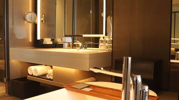 A modern bathroom with a large mirror, a bathtub, and a countertop with toiletries.