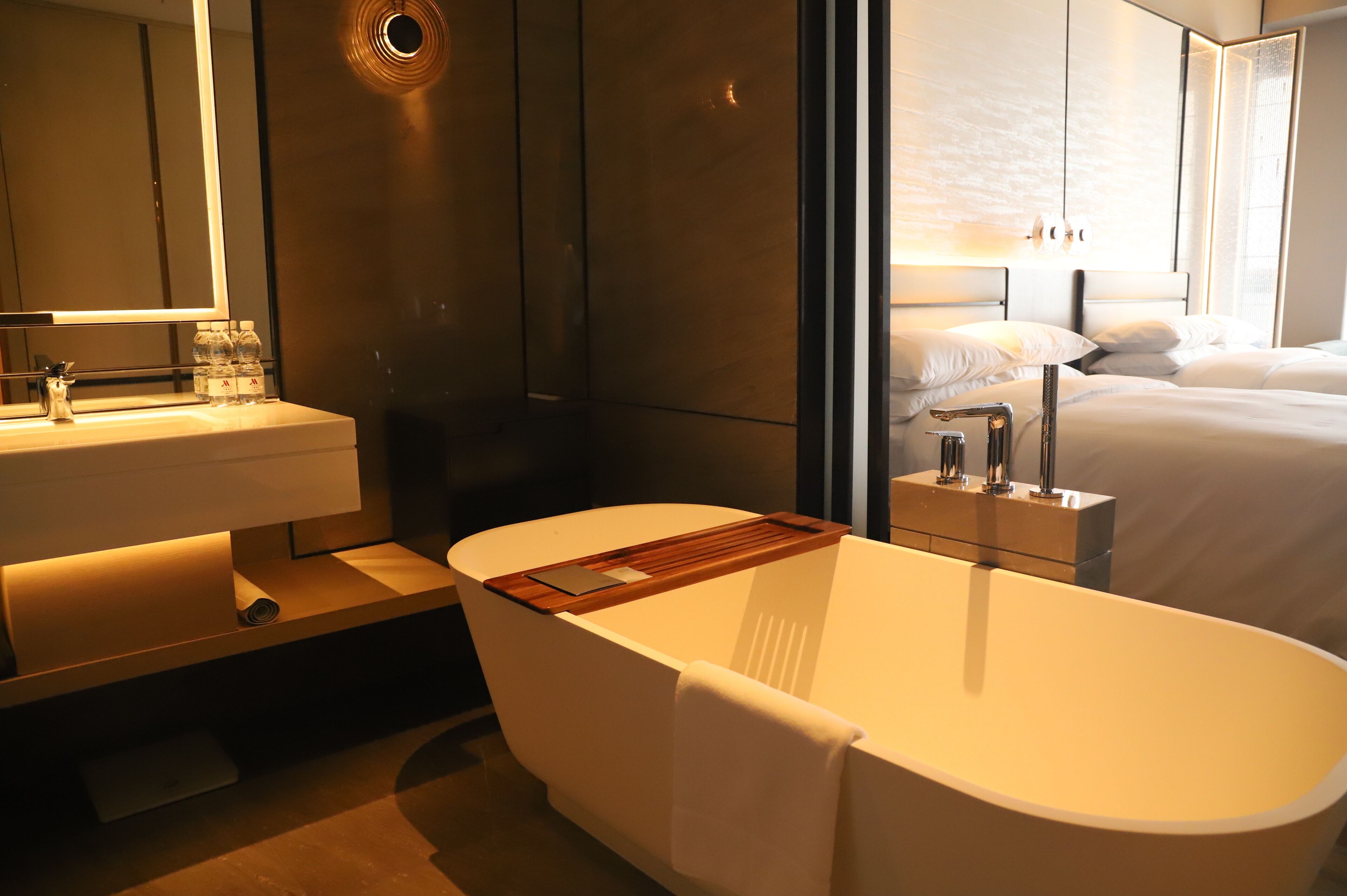 A modern bathroom with a freestanding bathtub, a vanity with a mirror, and a bedside table with a lamp.