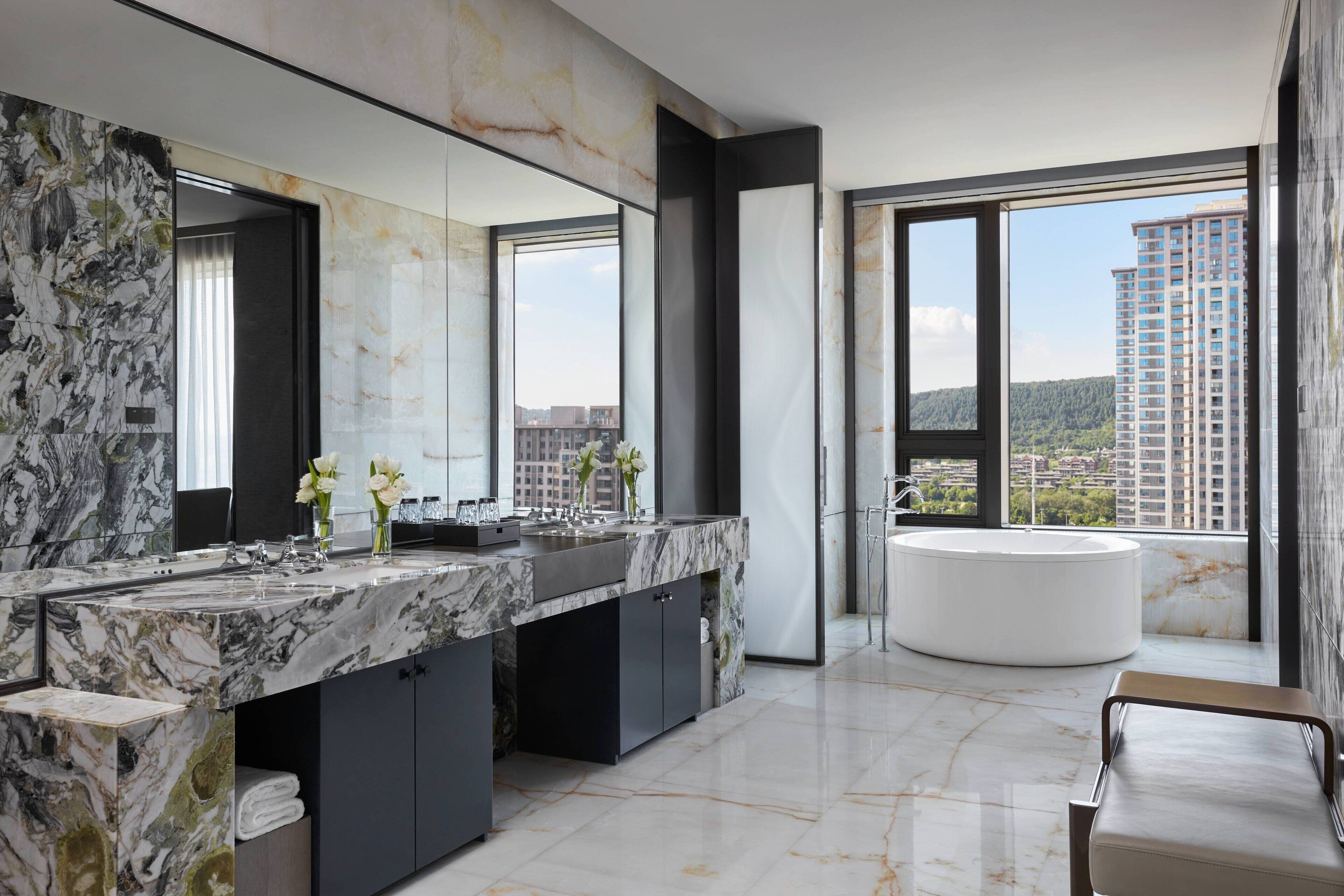 Un baño moderno con tocador de mármol, un espejo grande y una bañera independiente.