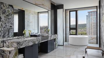 Un baño moderno con tocador de mármol, un espejo grande y una bañera independiente.