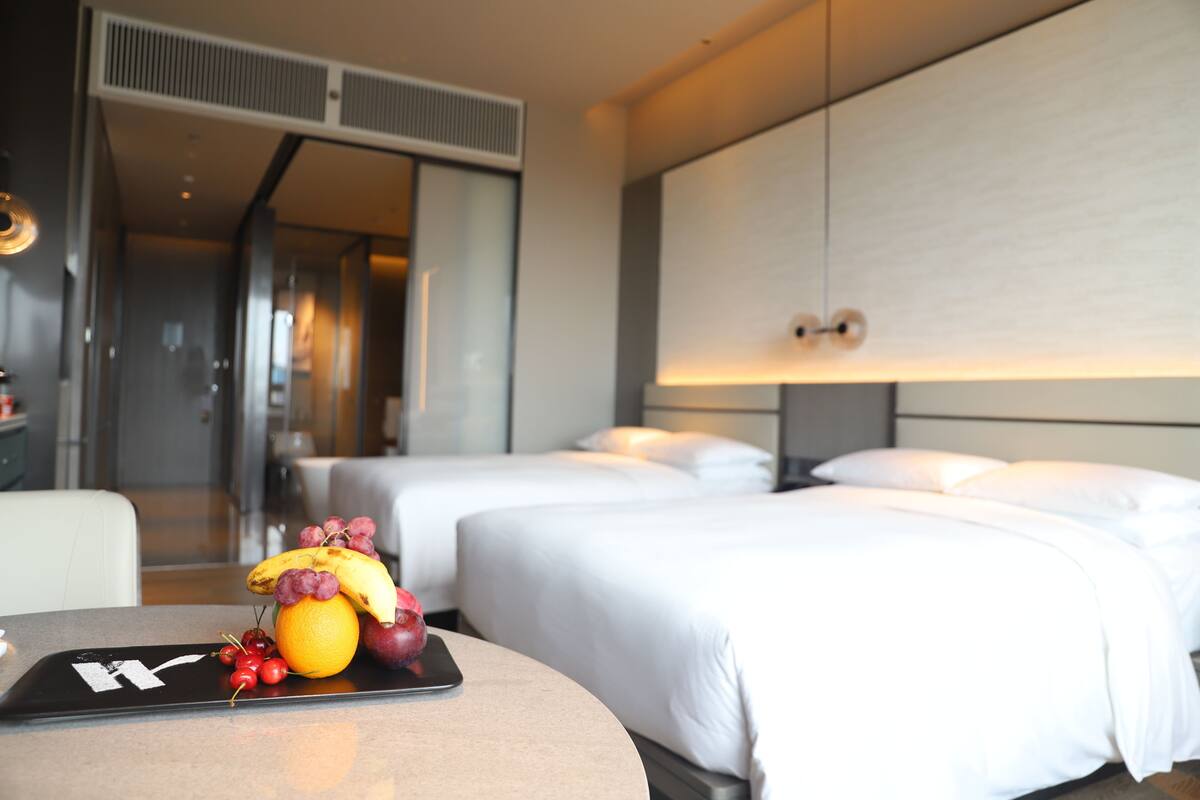 A hotel room with two beds, a bedside table with fruit, and a modern design.