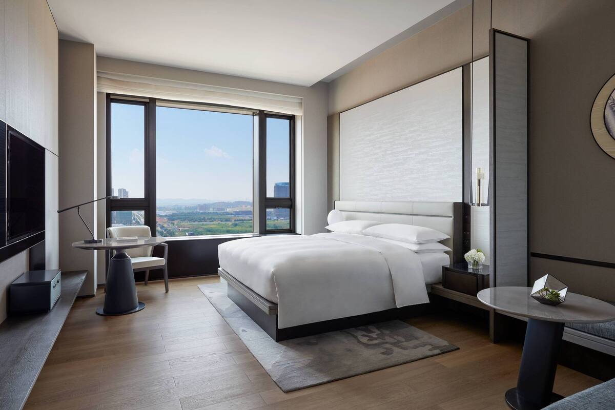 A modern hotel room with a large bed, a desk, a chair, and a TV.