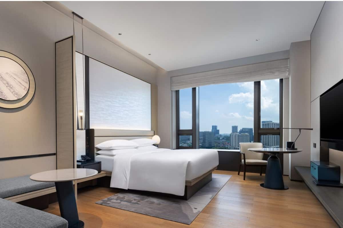 A modern hotel room with a large bed, a desk, a chair, and a TV.