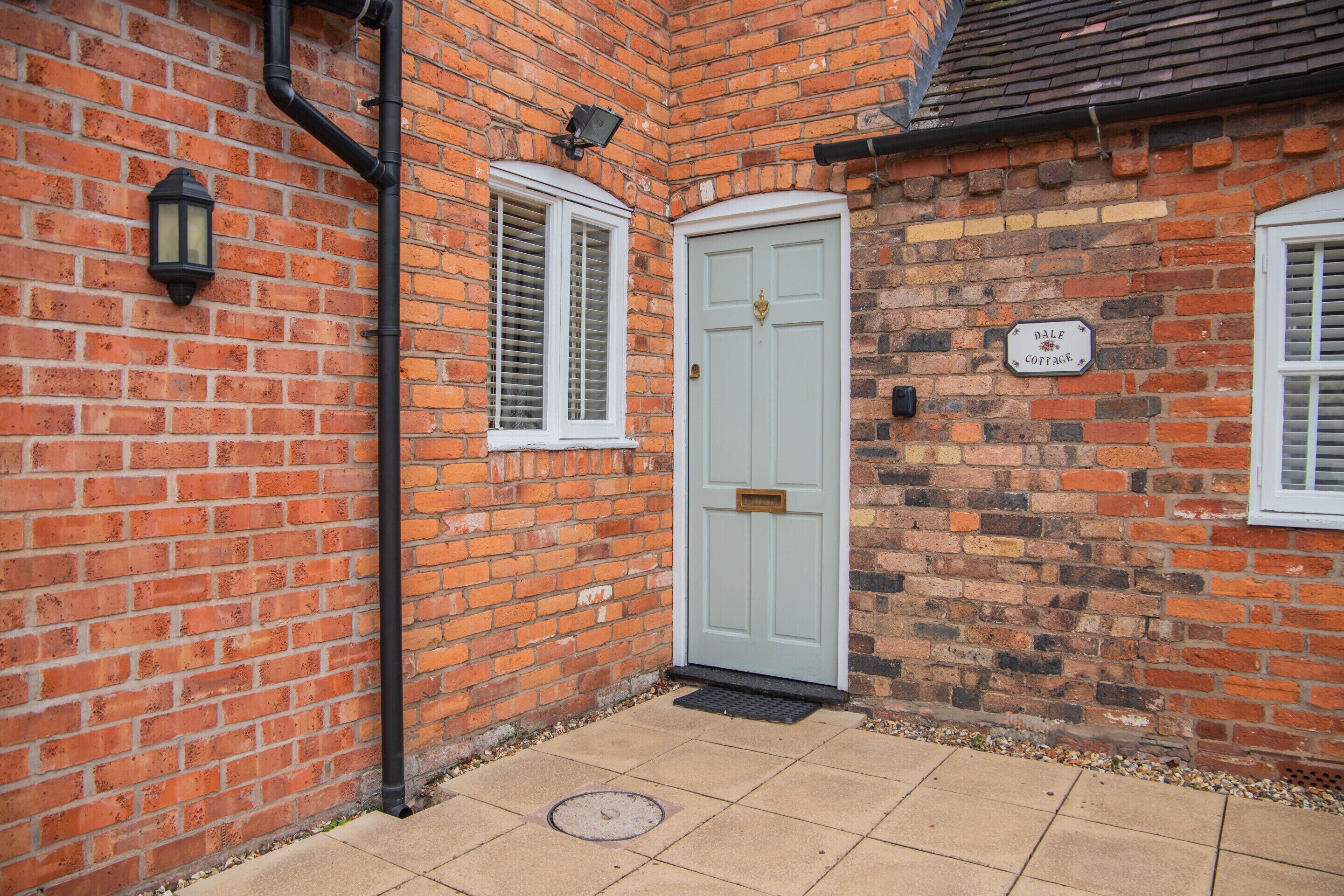 A corner of a building with a white door, a window with shutters, and a sign that reads 'Dale Cottage'.