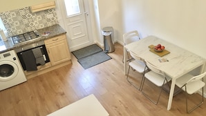 Cozinha compacta com máquina de lavar, fogão e área de refeições com mesa e cadeiras.