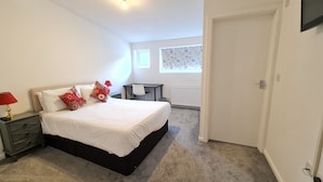 Quarto com cama, mesas de cabeceira, escrivaninha e janela.