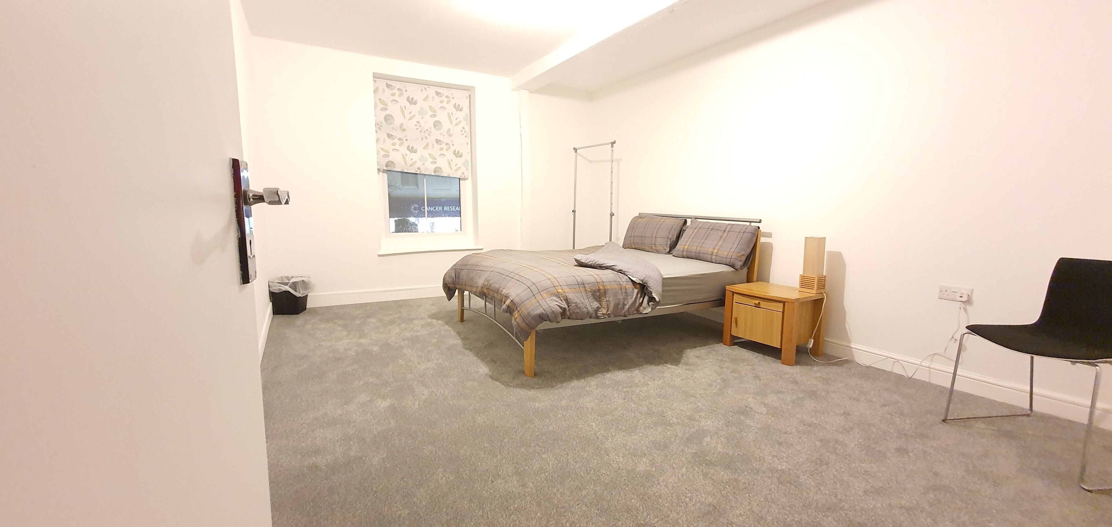 Une chambre à coucher comprenant un lit, une table de chevet, une chaise et une fenêtre avec des stores.