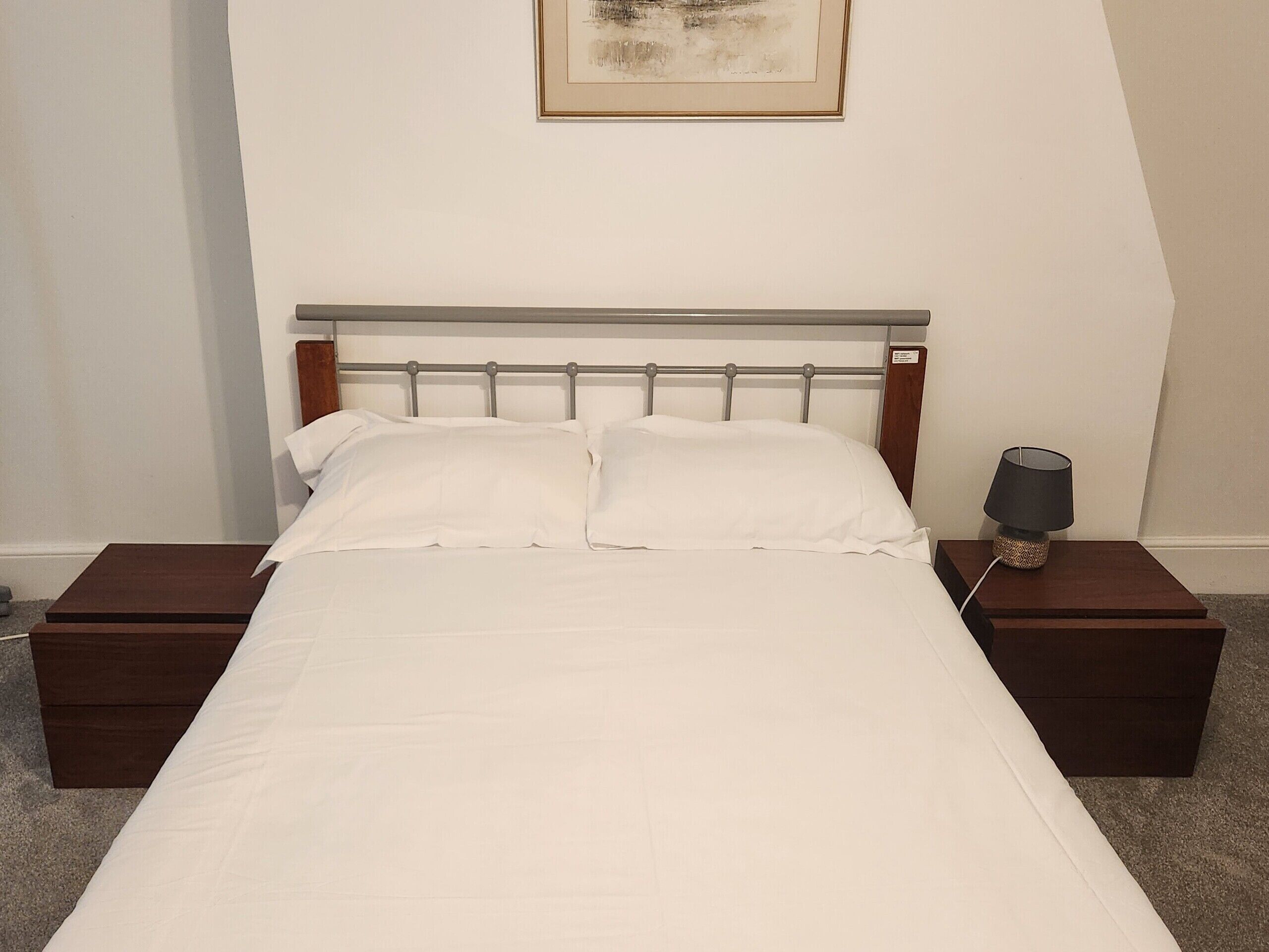 A neatly made bed with white linens in a room with a simple, modern design.