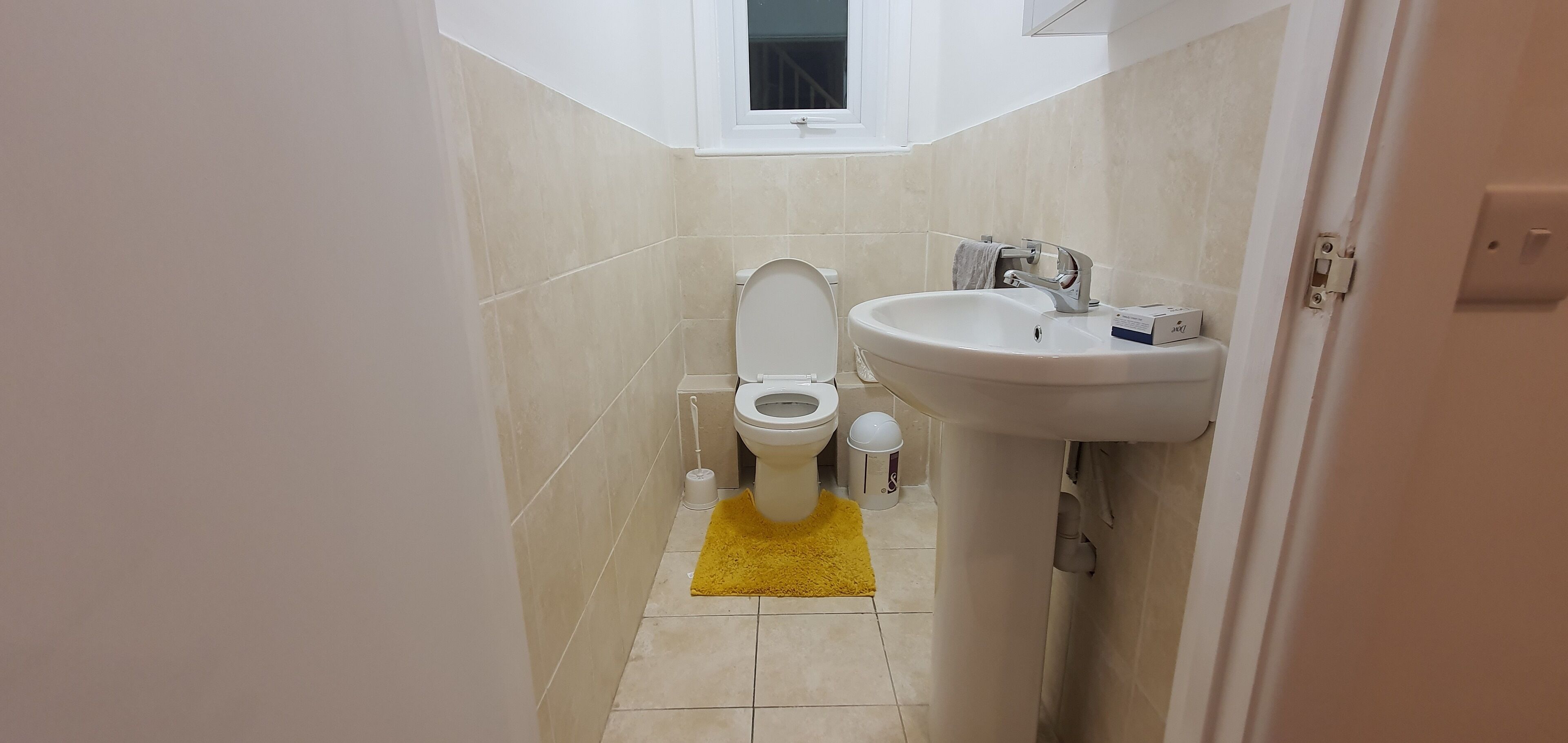 Een kleine badkamer met toilet, wastafel en een gele mat.