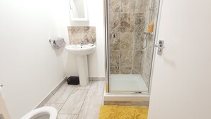 Un baño con un lavabo blanco, una cabina de ducha de cristal y una alfombra amarilla.