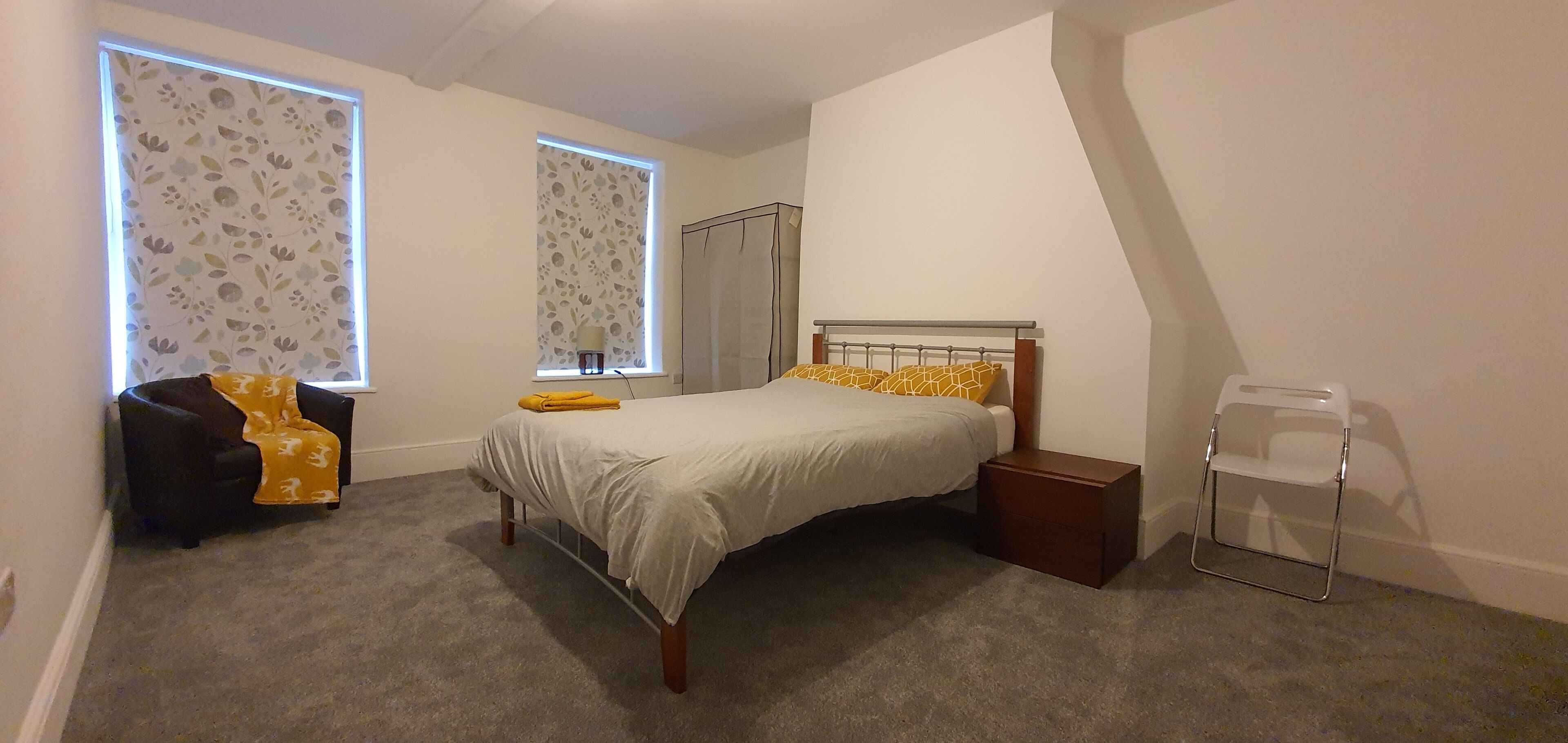 Un dormitorio con cama, una silla, una mesita de noche y una ventana con cortina.