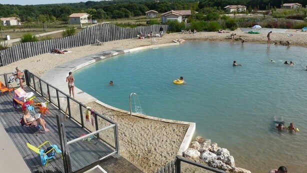 Una piscina con bordo in legno, circondata da una spiaggia di sabbia e una recinzione in legno.