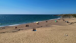 Ampia spiaggia sabbiosa con persone che prendono il sole e nuotano, e cielo azzurro terso.