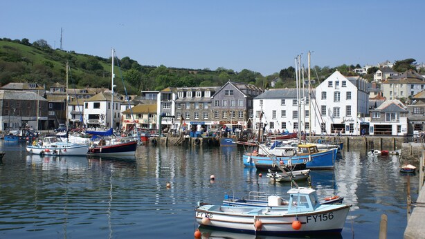 A harbor with boats docked, buildings in the background, and a hilly landscape. - Harbourside Apartment (St Austell)