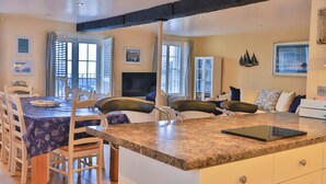 A modern kitchen with a granite countertop, a dining area with a table and chairs, and a living area with a sofa and a TV. - Harbourside Apartment (St Austell)