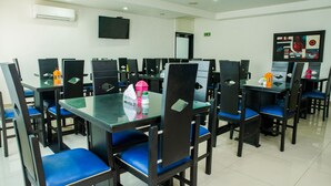 A dining area with multiple tables and chairs, a flat-screen TV mounted on the wall, and an air conditioning unit above the tables.