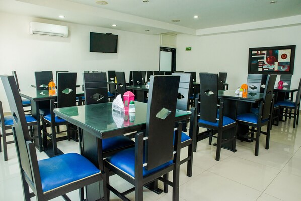 A dining area with multiple tables and chairs, a flat-screen TV mounted on the wall, and an air conditioning unit above the tables. - Ayenda 1315 Candiac (Barranquilla)
