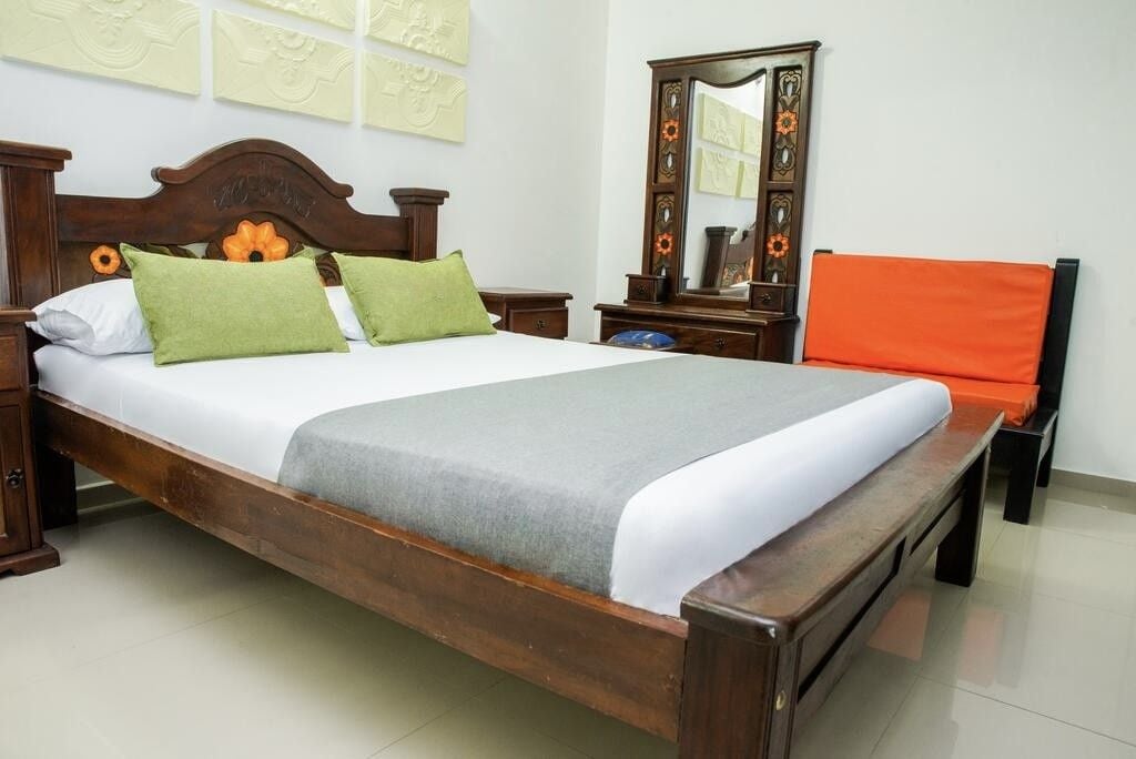 A wooden bed with a headboard, two pillows, a nightstand, a mirror, and an orange chair.