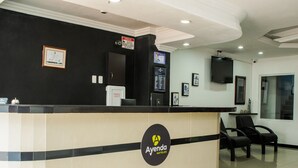 A hotel reception desk with a logo, a framed certificate, a digital screen, and a television.