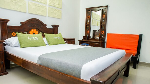A neatly made bed with green pillows, a wooden headboard, and a nightstand with a mirror.