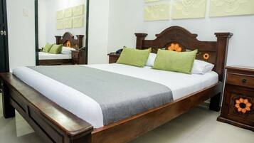 Cama bem arrumada com cabeceira de madeira, mesa de cabeceira com detalhe floral e espelho na parede.