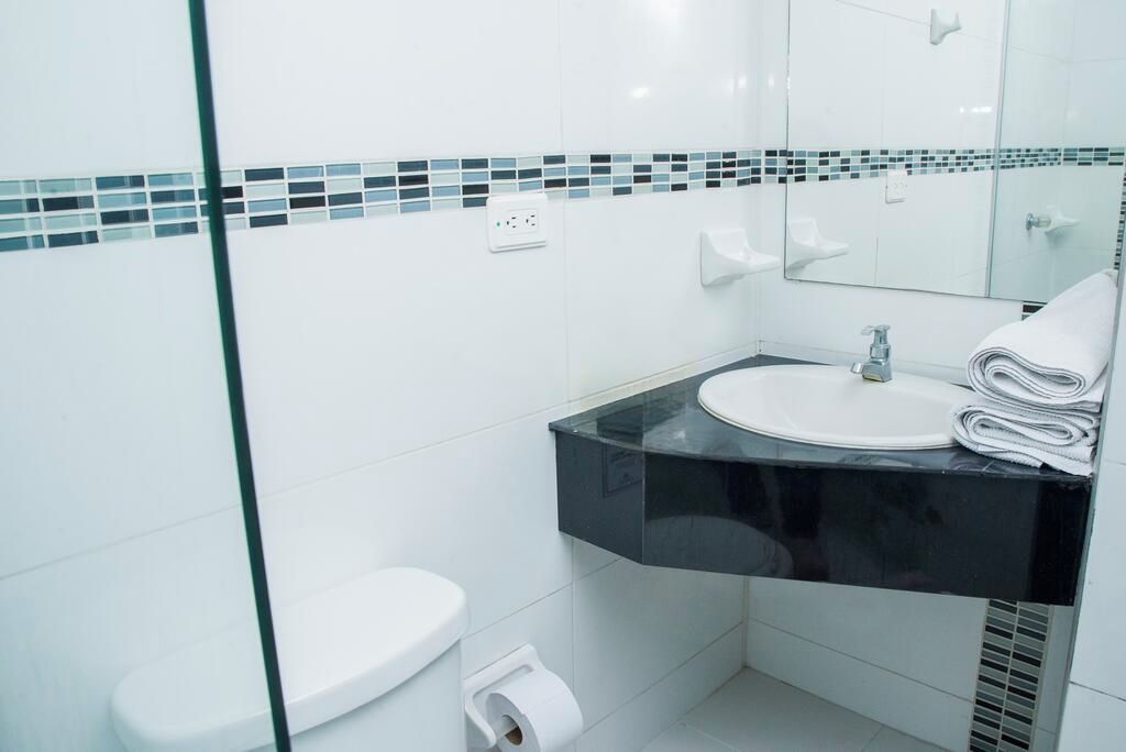 A modern bathroom with a glass partition, a white toilet, a black countertop with a sink, and a mirror.