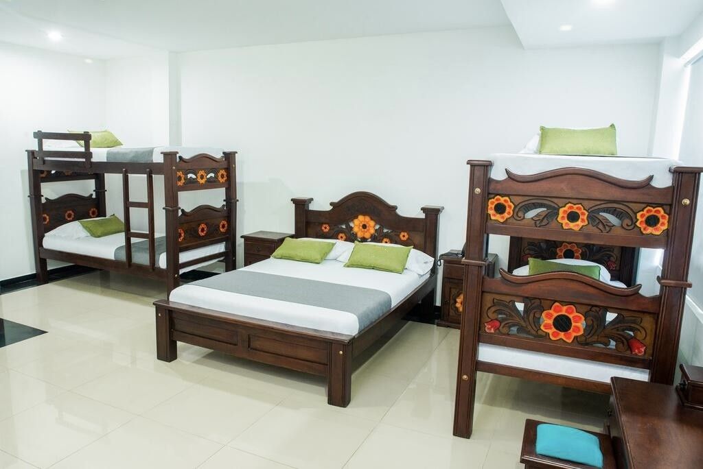 Una habitación de hotel con una cama grande, dos camas más pequeñas y una mesita de noche de madera.