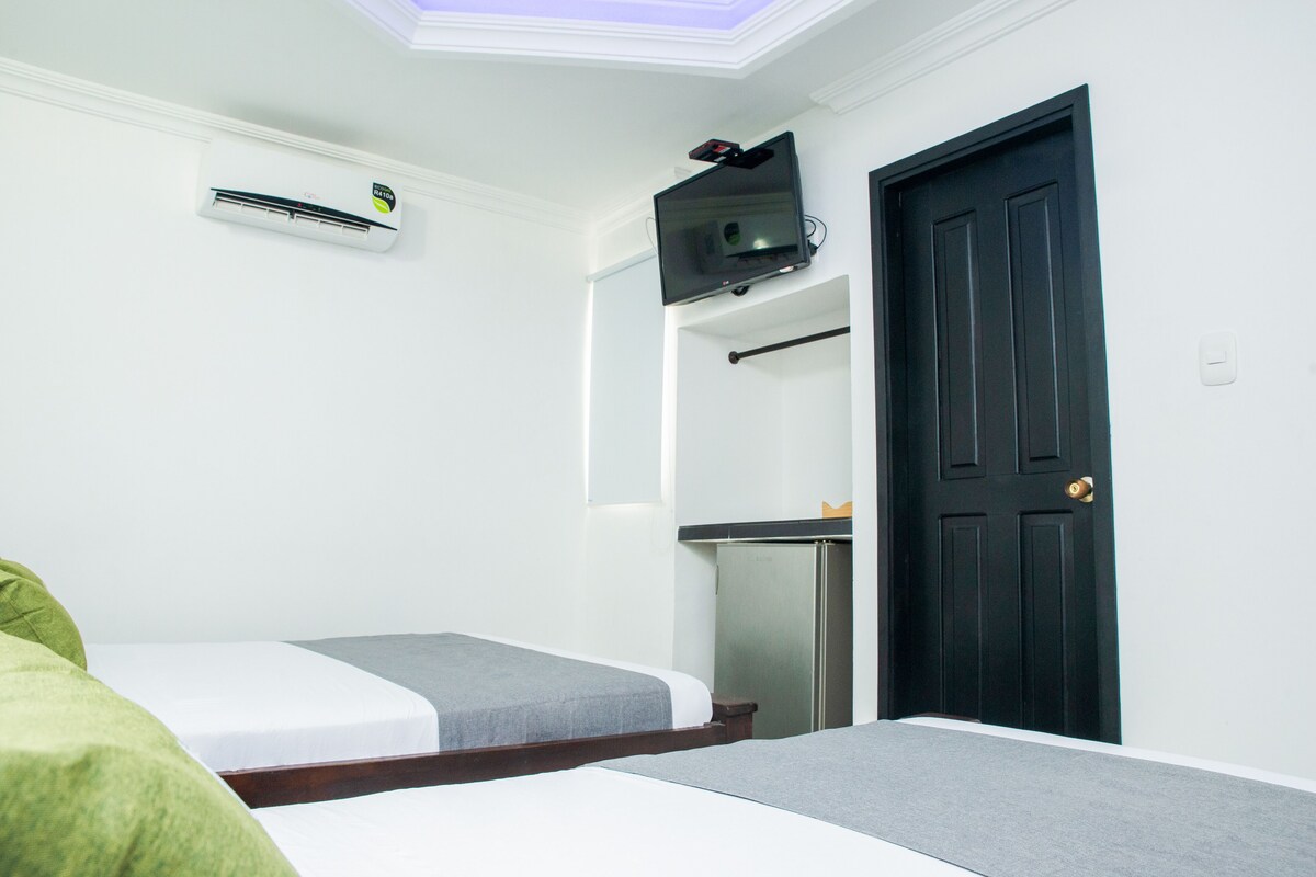 A room with two beds, a black door, a TV mounted on the wall, and a small refrigerator.