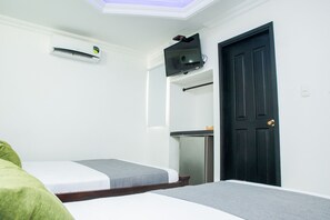 Een kamer met twee bedden, een zwarte deur, een aan de muur bevestigde televisie en een kleine koelkast.