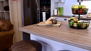 A kitchen island with a cutting board, bread, and a fruit basket. - River Mist (Telford)