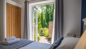 A bedroom with a large bed, a wooden door, and a view of a garden through an open door. - River Mist (Telford)