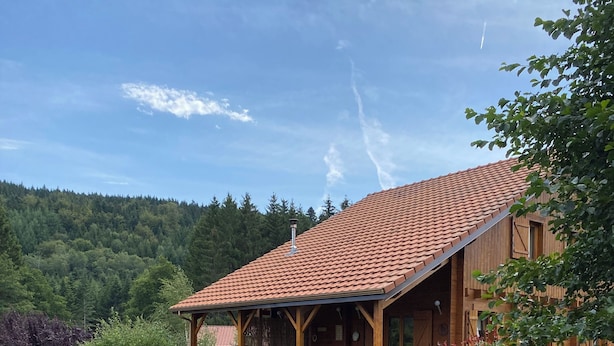 En stuga byggd av trä med ett tak täckt av tegelpannor, en inglasad veranda och en damm.