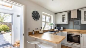 Una cocina moderna con encimera de madera, armarios blancos, horno integrado y un reloj en la pared.