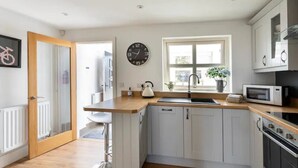 Una cocina moderna con armarios blancos, encimera de madera, microondas, horno y un reloj en la pared.