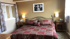 Een net opgemaakt bed met een beddekleed met dessin, twee nachtkastjes met lampen, een ingelijst schilderij aan de muur en een raam met gordijnen.