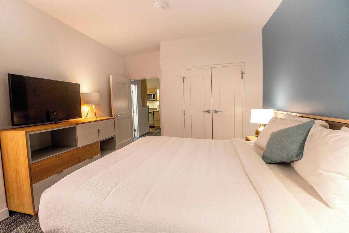 A hotel room with a large bed, a TV, a desk with a lamp, and a wardrobe.