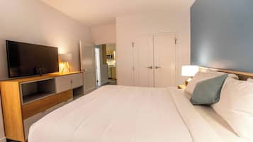 A hotel room with a large bed, a TV, a desk with a lamp, and a wardrobe.