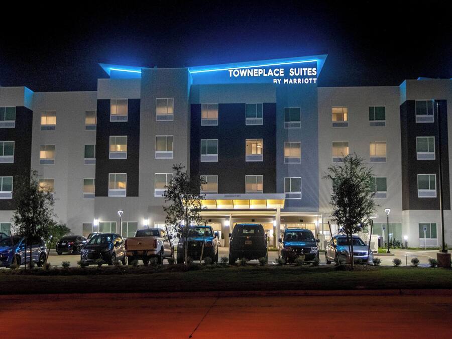 Un hotel de varios pisos, un estacionamiento con varios automóviles y un letrero que indica que es un TownePlace Suites by Marriott.