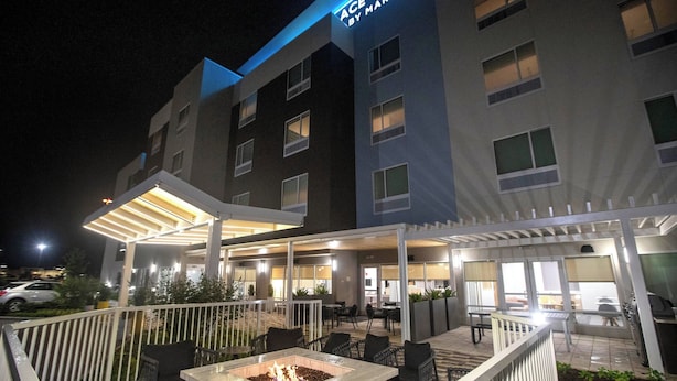 A hotel exterior with a covered outdoor seating area, a fire pit, and a sign reading "ACE Suites by Marriott." - TownePlace Suites by Marriott Conroe (Conroe)