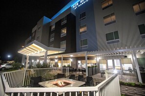 A hotel exterior with a covered outdoor seating area, a fire pit, and a sign reading "ACE Suites by Marriott."