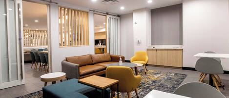 A modern lounge area with a sofa, chairs, a small table, and a dining table.
