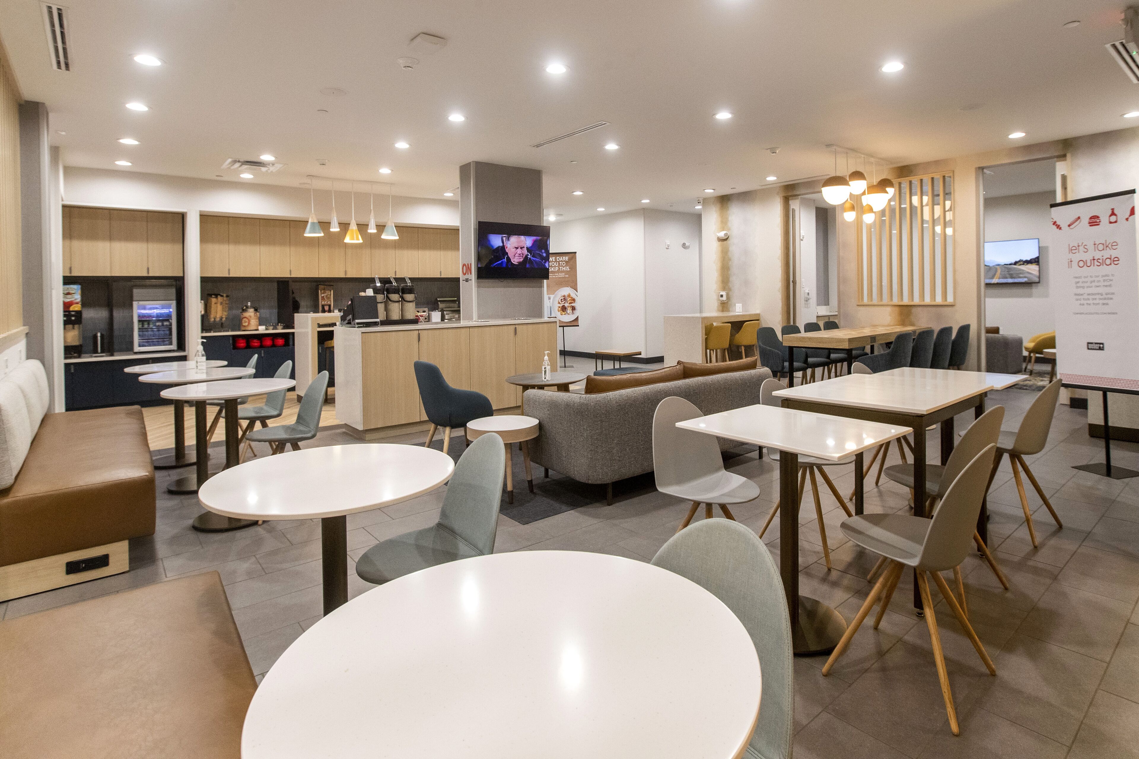 A modern restaurant with round tables, a bar area, and a television screen.