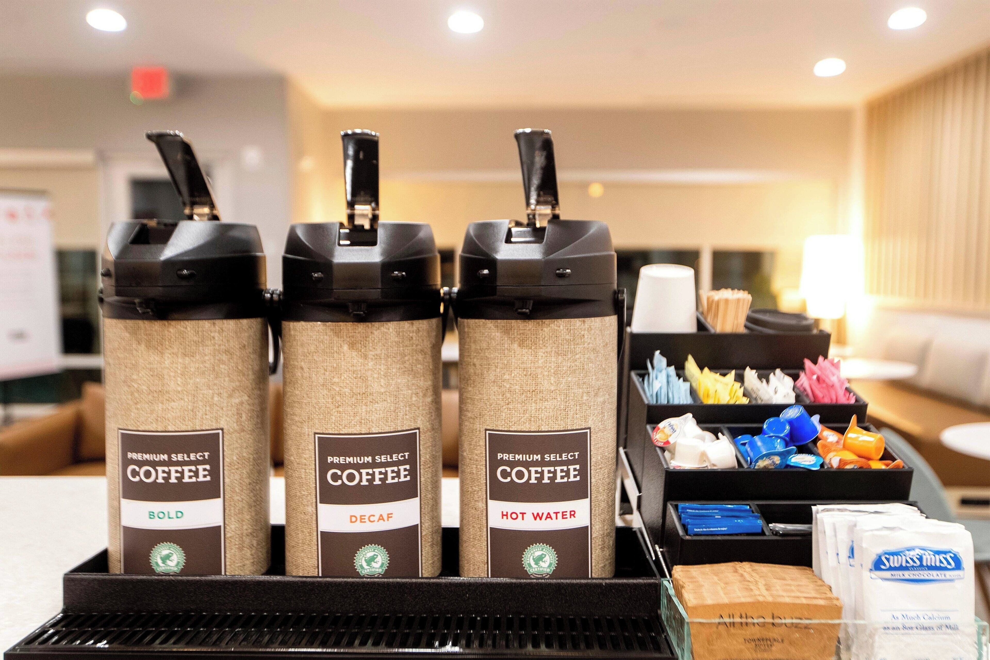 Una estación de café con tres dispensadores etiquetados como 'Premium Select Coffee' en negrita, opción descafeinada y agua caliente.